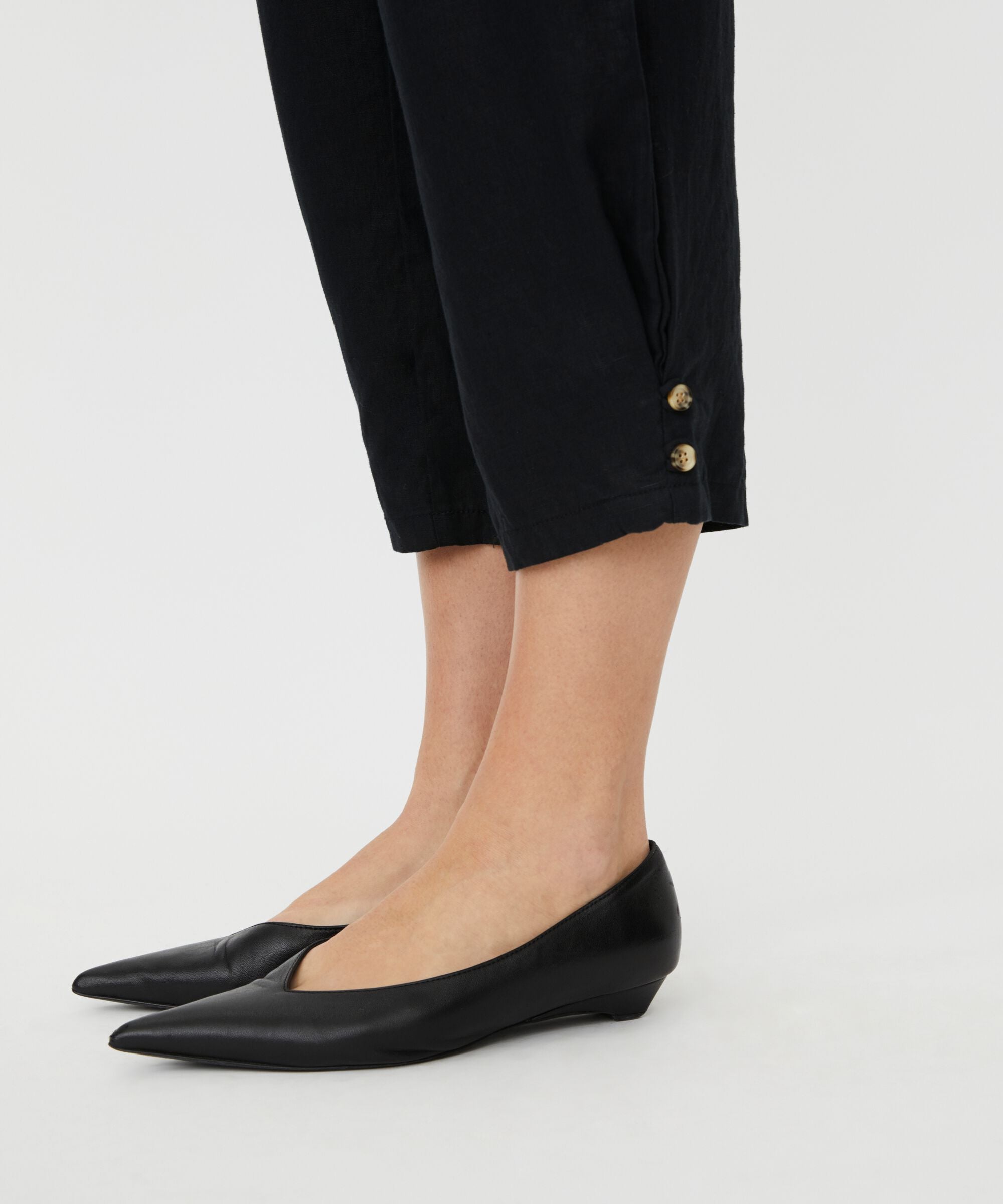 Black flat shoes worn with black pants on a light gray background