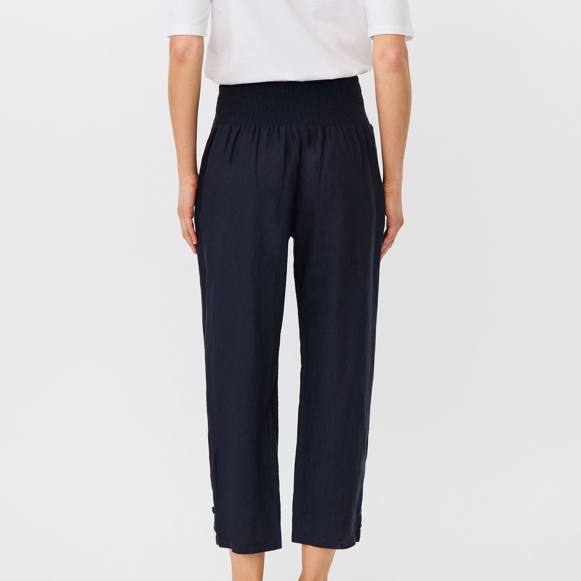 Person wearing navy pants and a white top on a light gray background