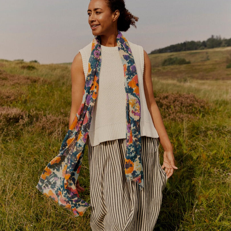 Floral print scarf draped around a woman wearing a cream knit top and striped skirt.
