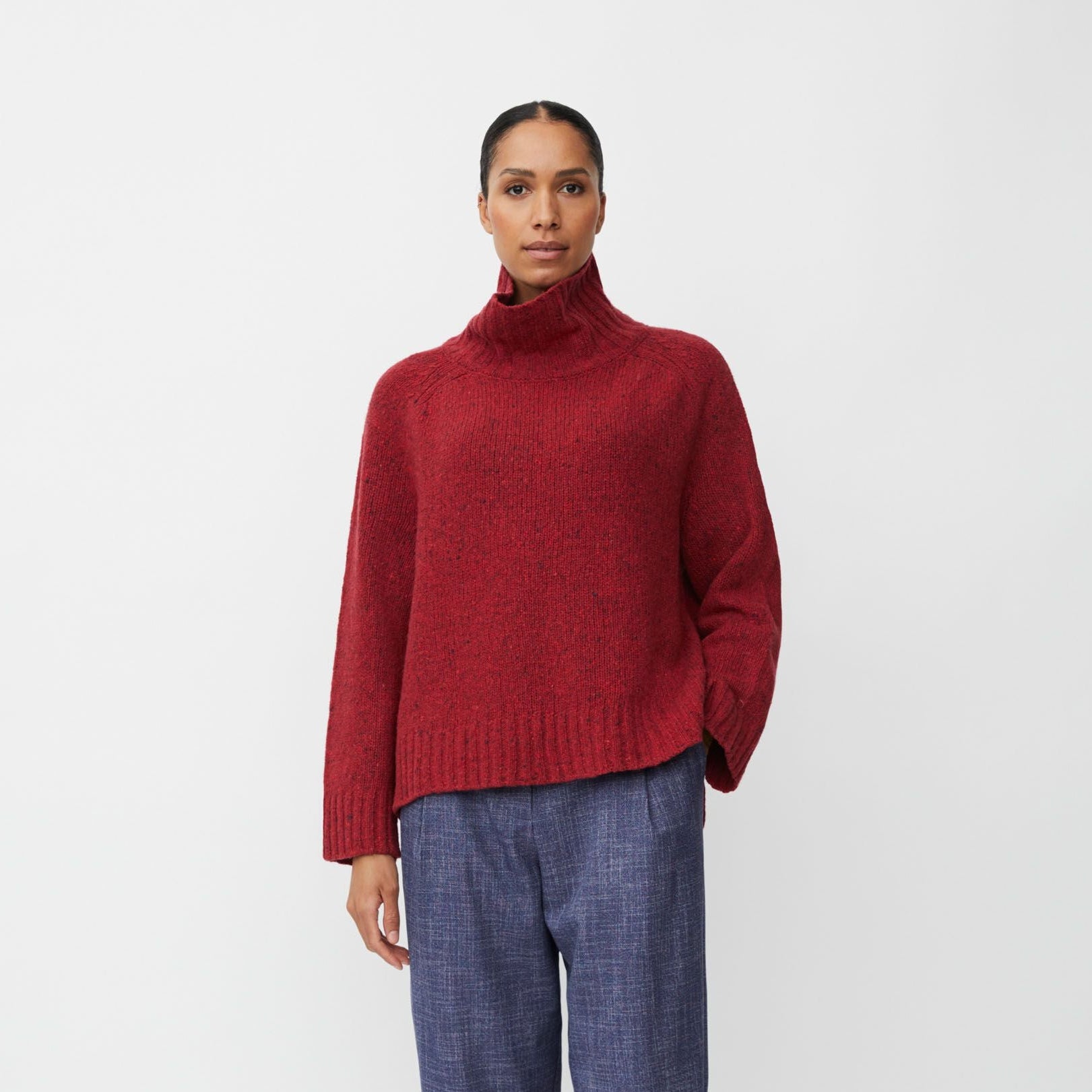 Person wearing a red turtleneck sweater and blue plaid pants on a white background