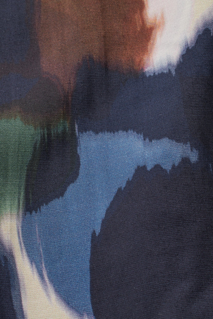 Close-up of dark navy fabric with an abstract print featuring shades of blue, brown, and green in a watercolor-like style.