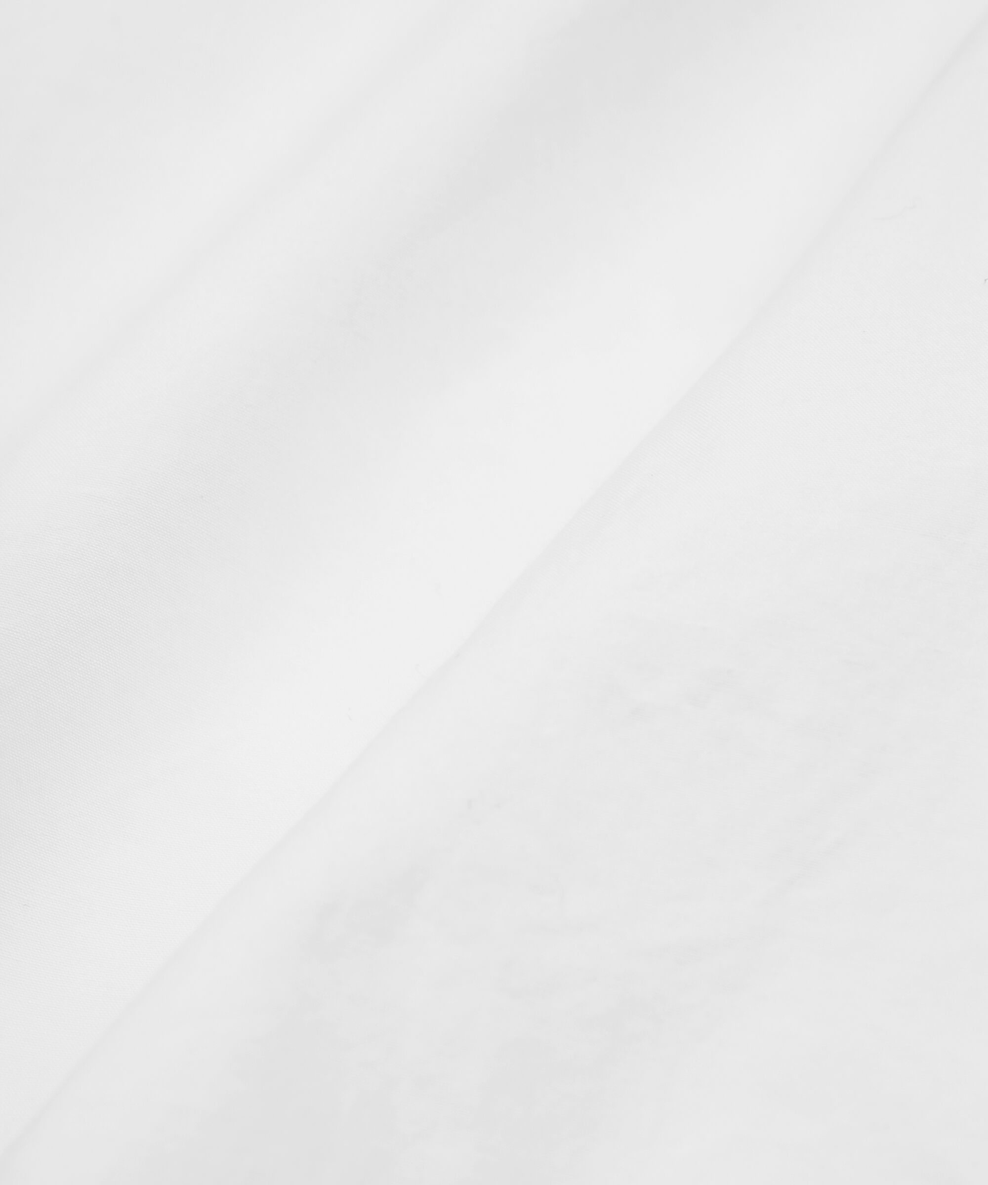 A close-up of a white textured fabric with soft diagonal folds and a slightly mottled surface.