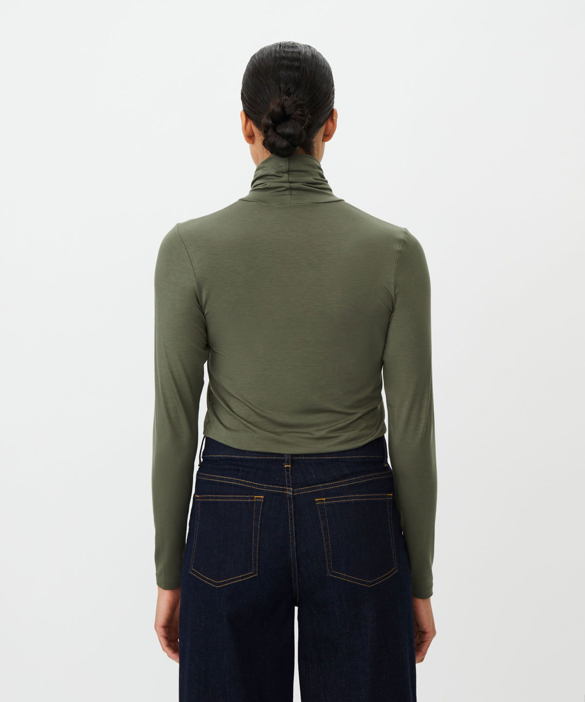 A model shown from the back wearing an olive green long-sleeve turtleneck top and dark blue jeans against a plain white background.