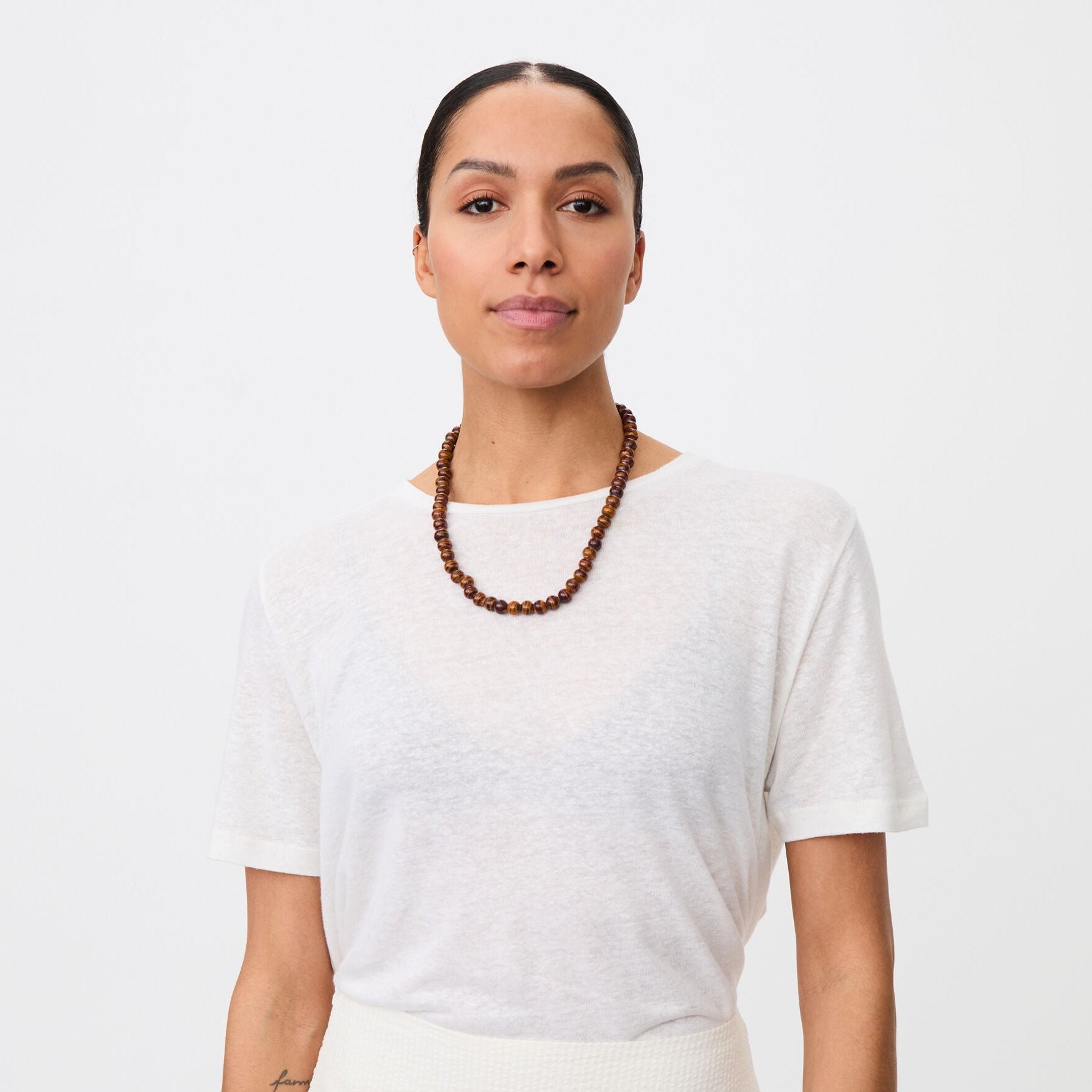 Woman wearing a white top and pleated skirt with a plain background