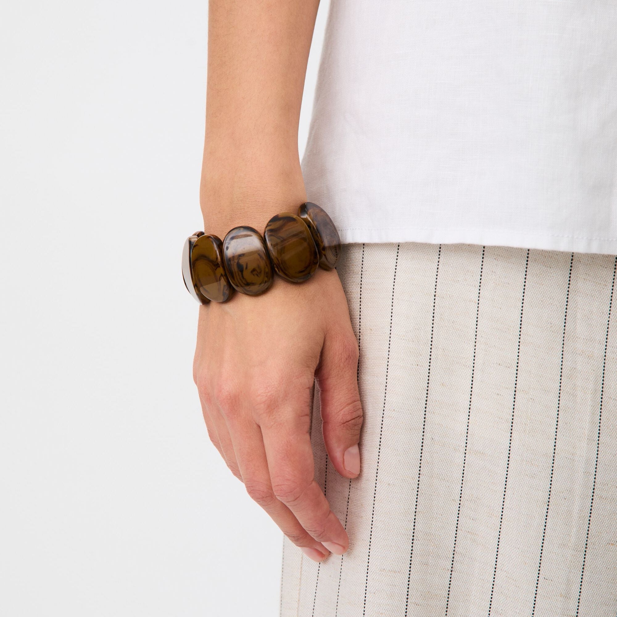 Hand wearing a brown beaded bracelet on a white background