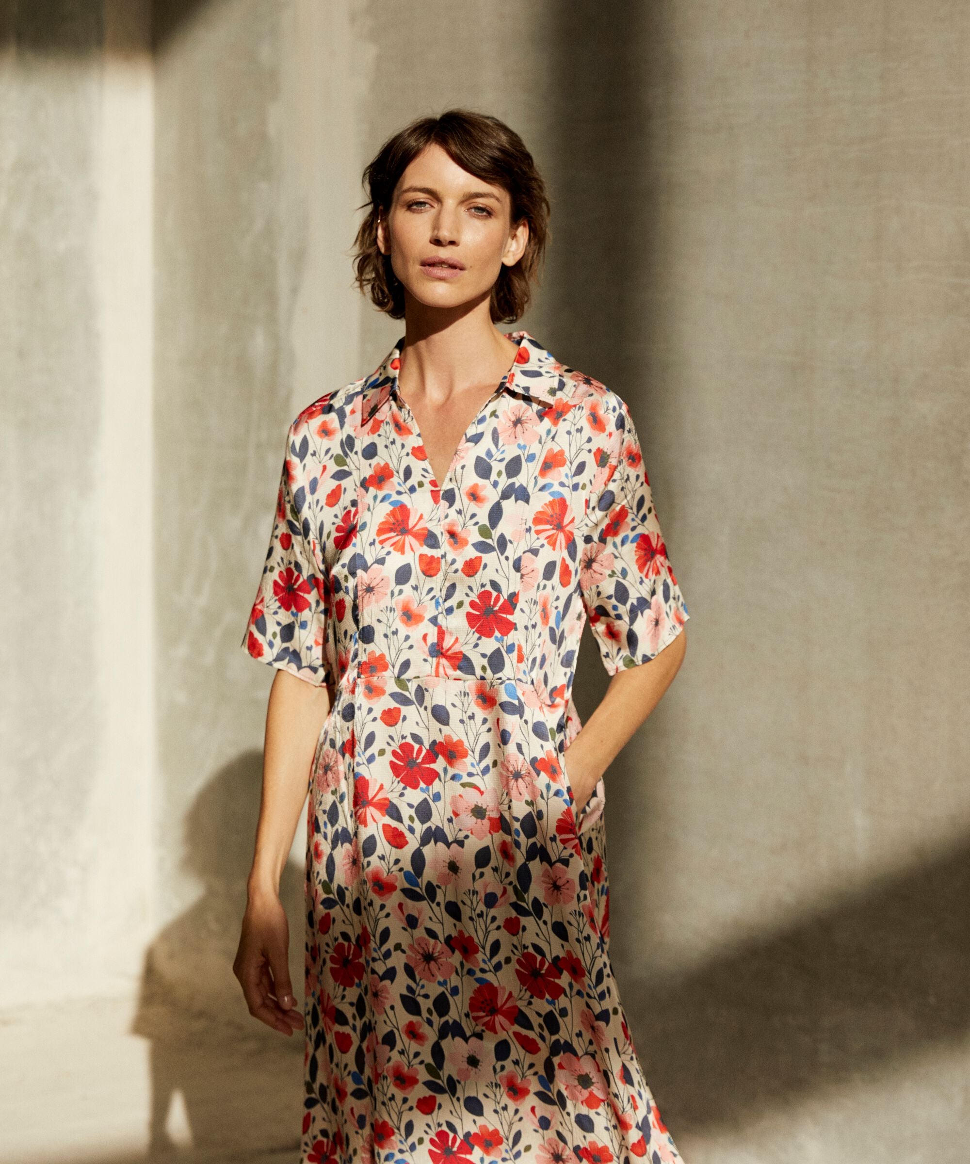 Woman wearing a floral dress standing against a textured wall.