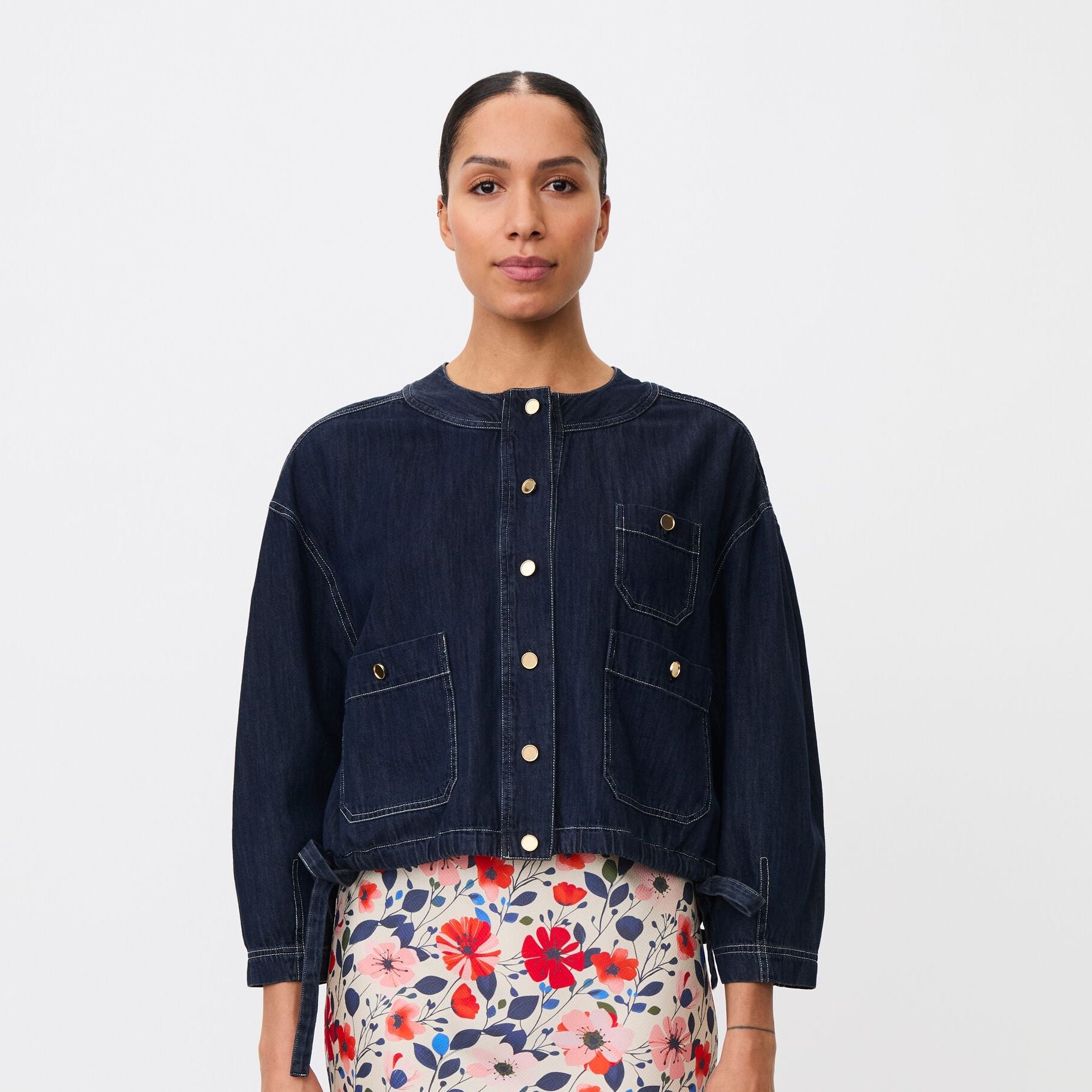 Woman wearing a dark denim jacket and floral skirt on a white background