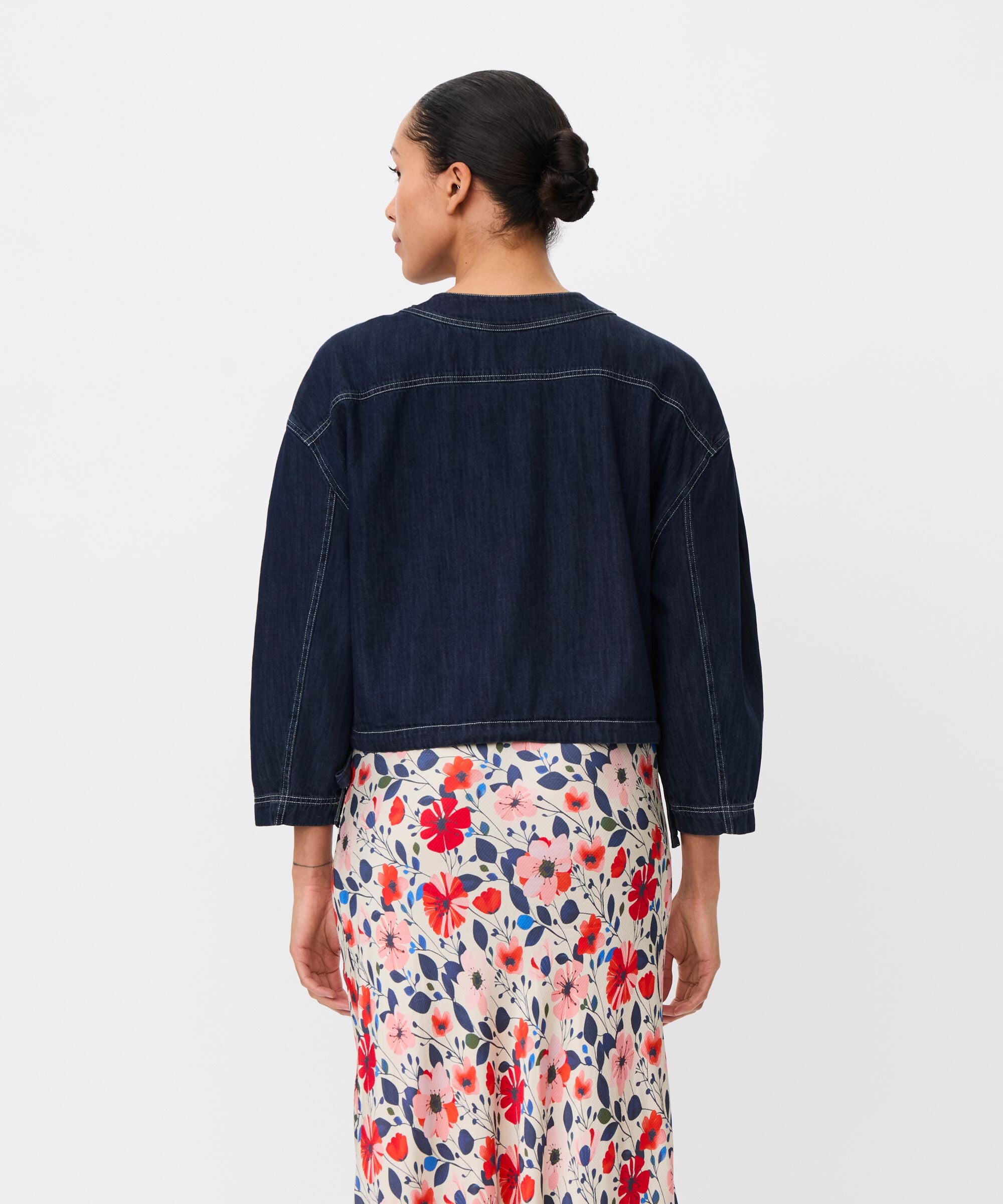 Person wearing a dark denim jacket and floral skirt on a white background