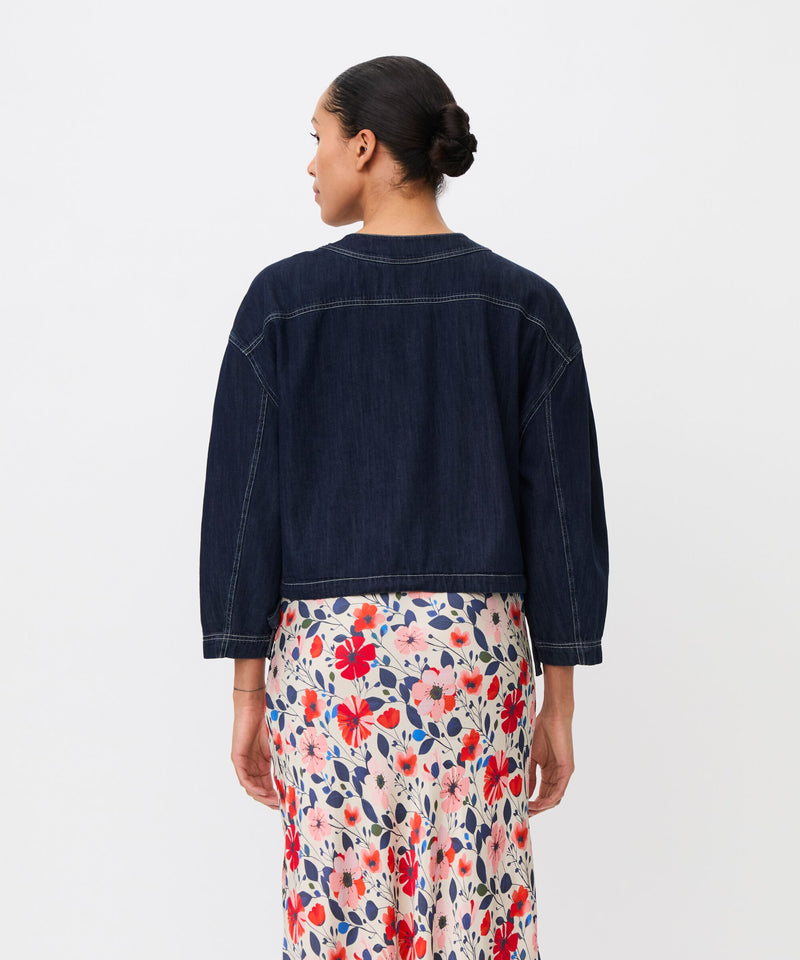 Person wearing a dark denim jacket and floral skirt on a white background