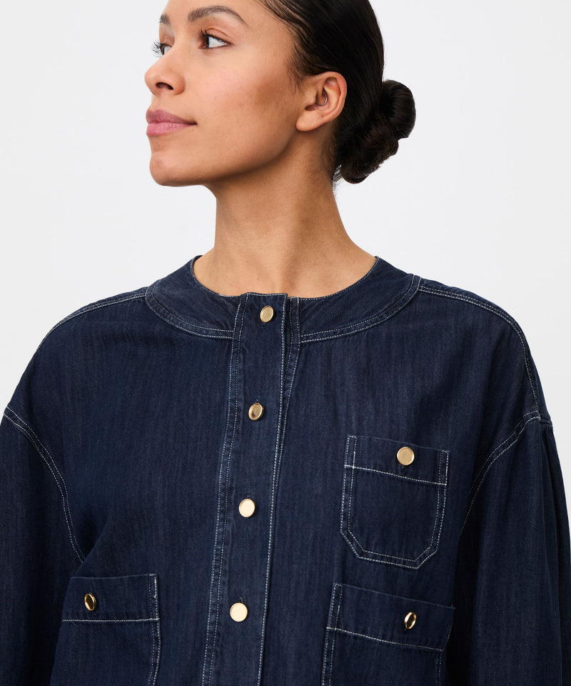 Woman wearing a dark denim shirt with a plain background