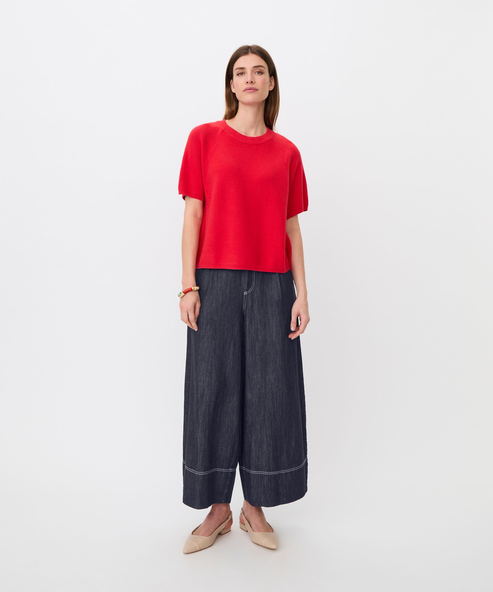 Woman wearing a red top and dark blue wide-leg pants on a white background