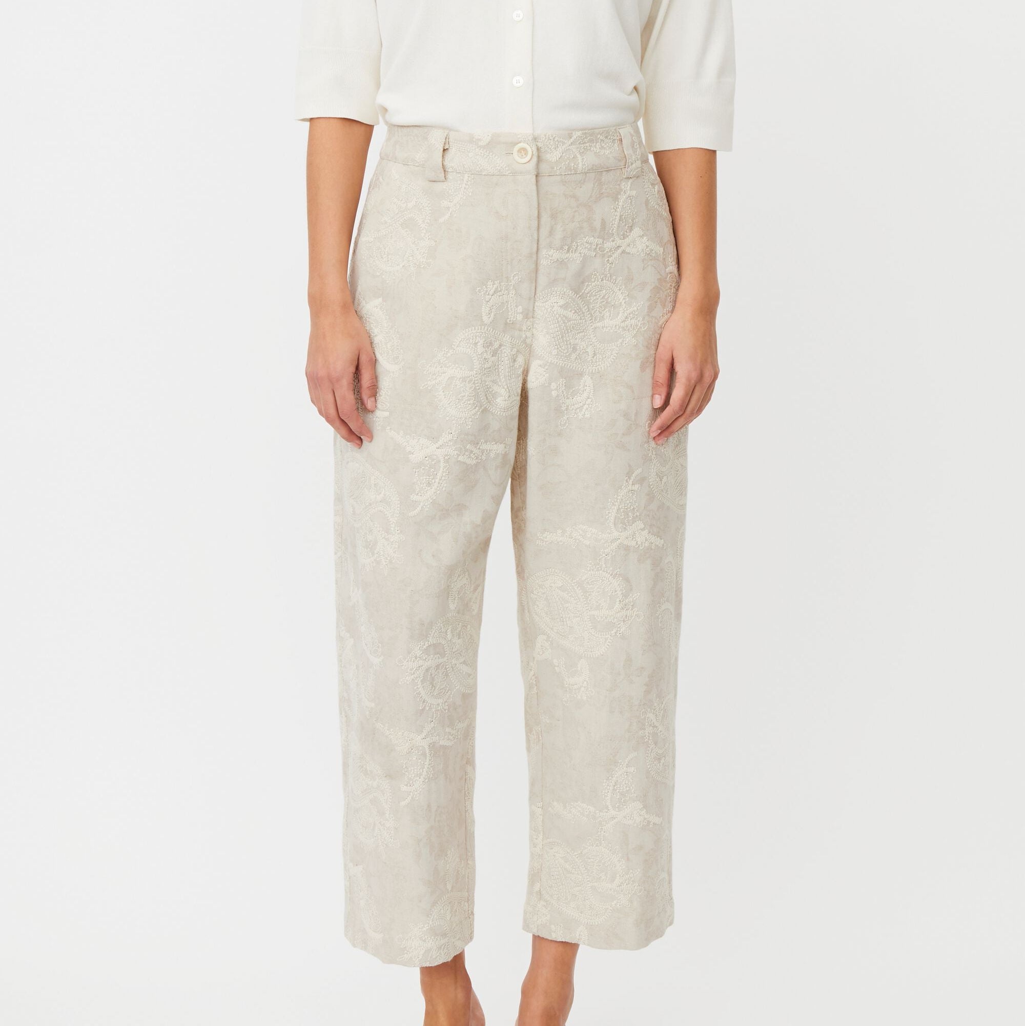 Person wearing beige patterned pants and a white shirt on a white background