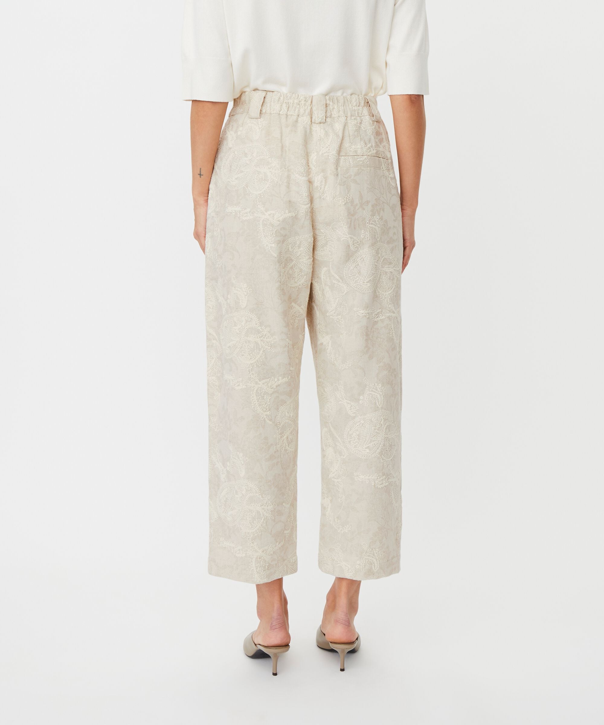 Person wearing beige wide-leg pants and a white top on a white background