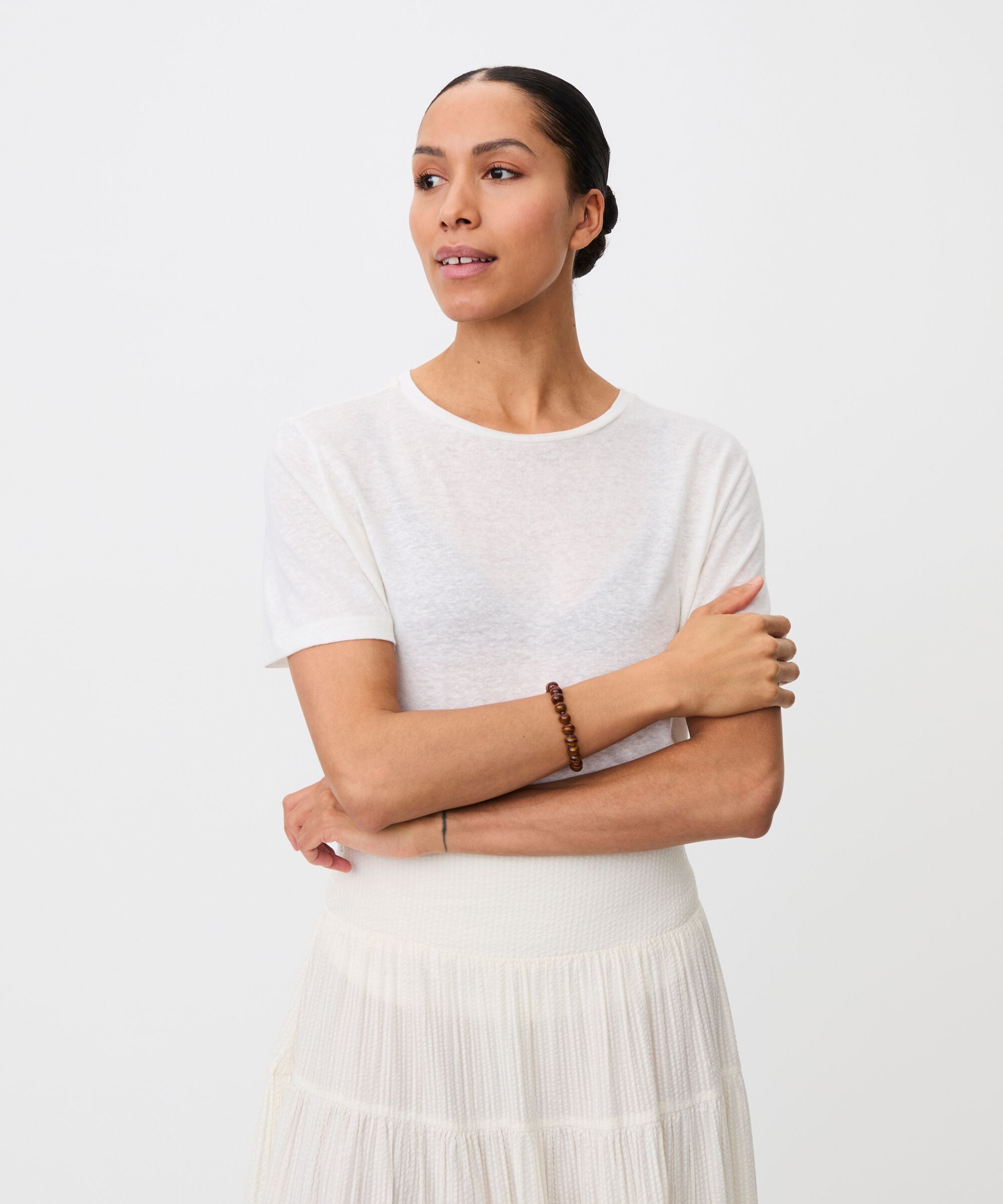 Woman wearing a white top and skirt with arms crossed on a plain background
