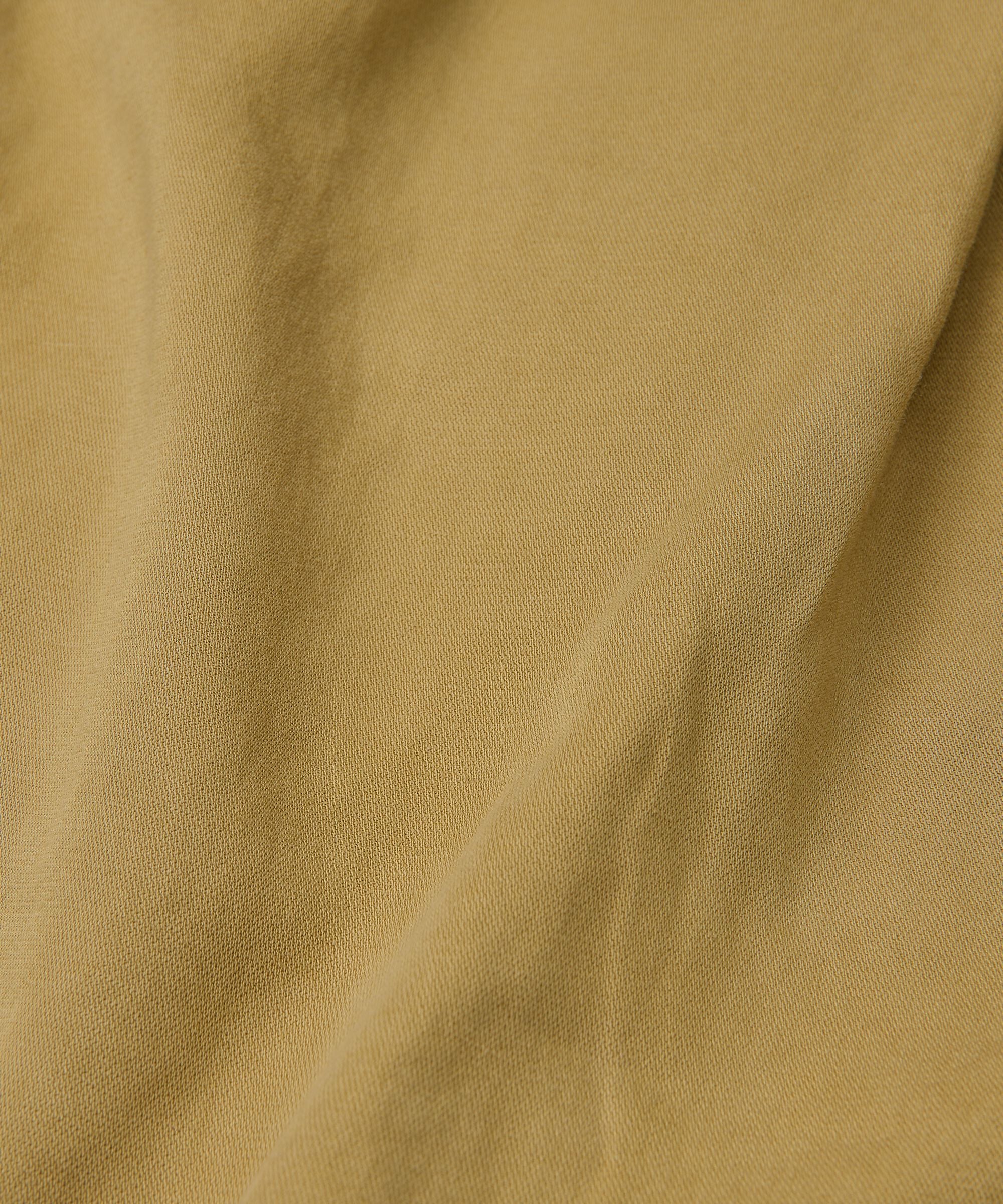 A close-up of draped fabric in a warm mustard yellow or ochre color, showing the soft texture and subtle folds.
