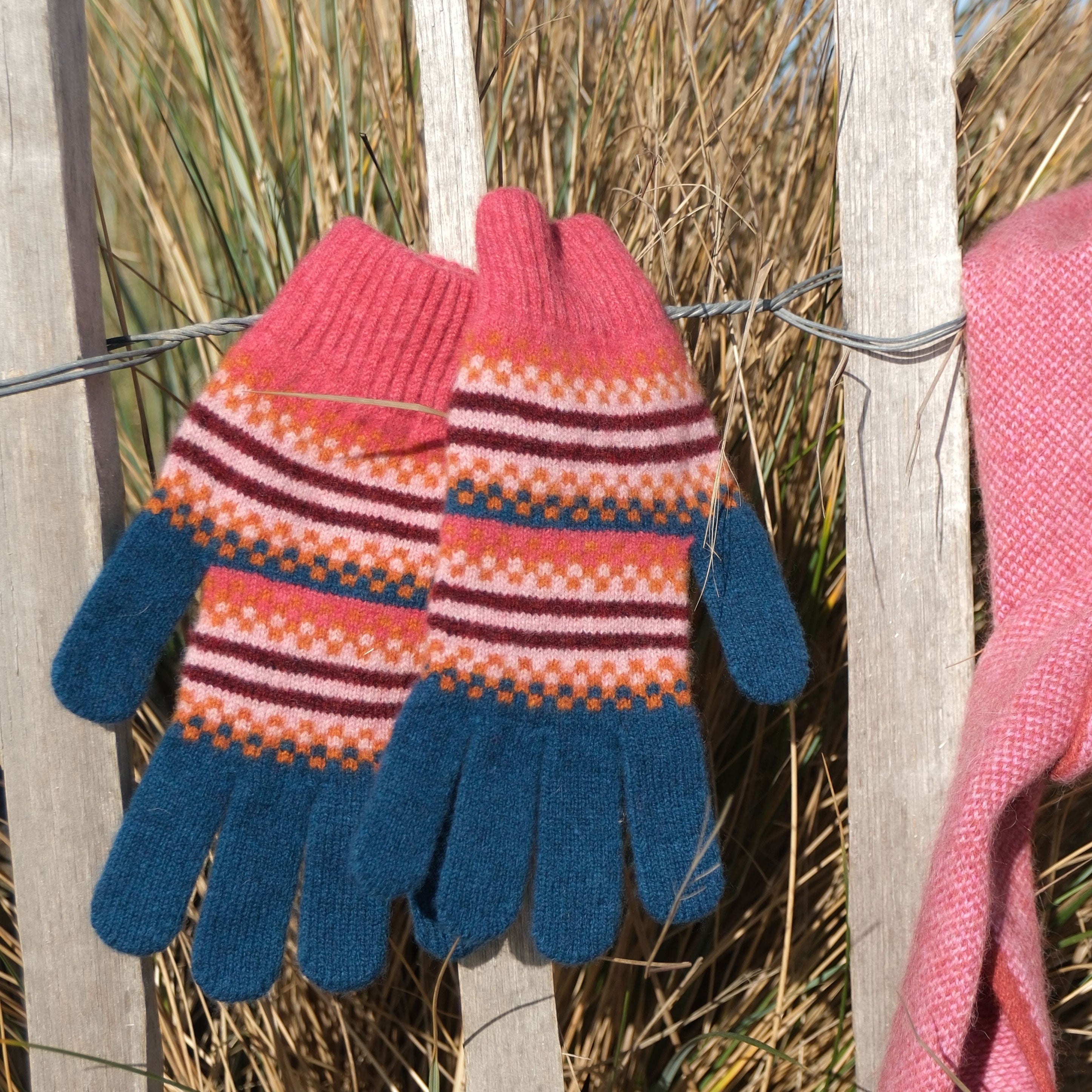 Pair of colorful knitted gloves hanging on a wooden fence with grass in the background