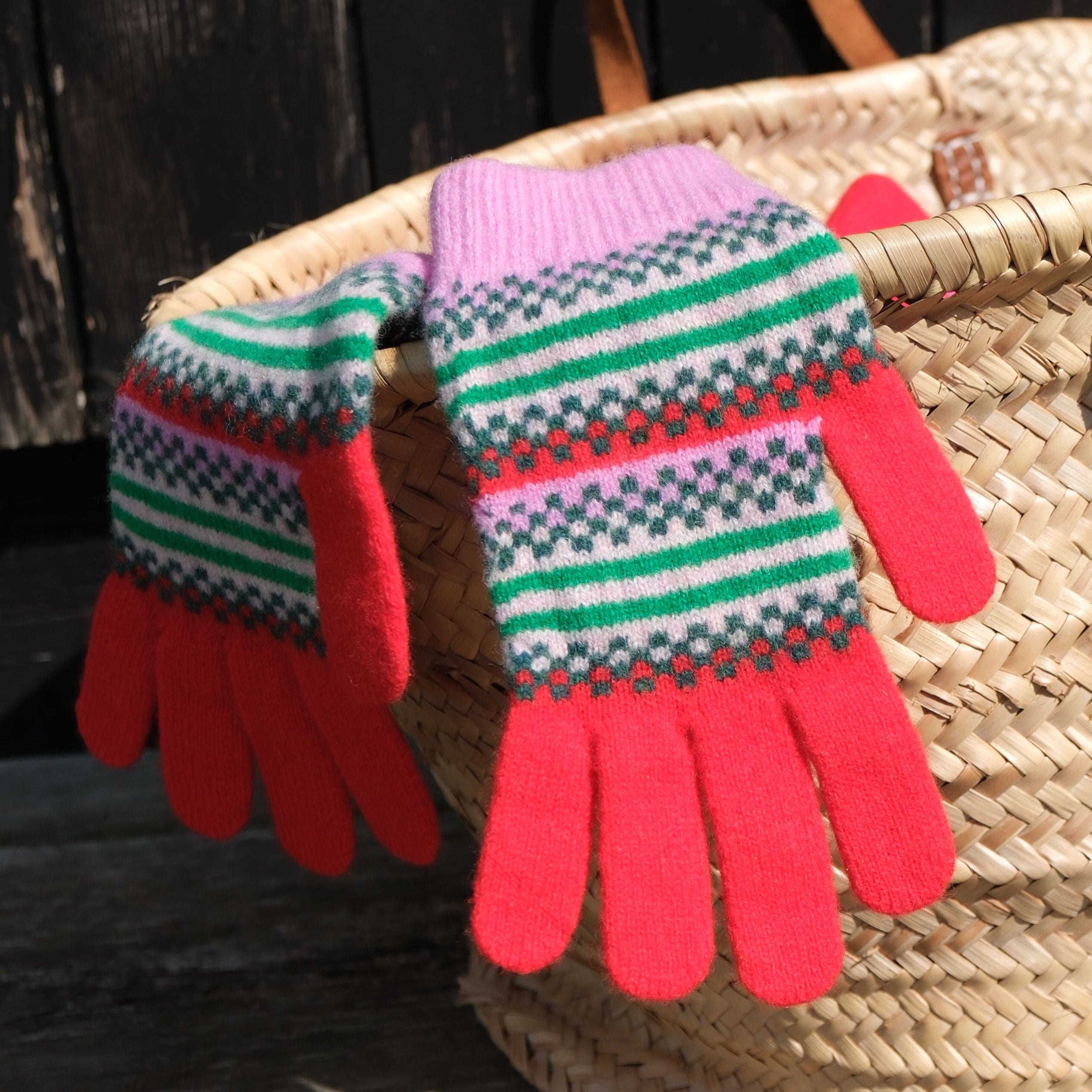 Pair of red and patterned gloves on a woven basket against a wooden background