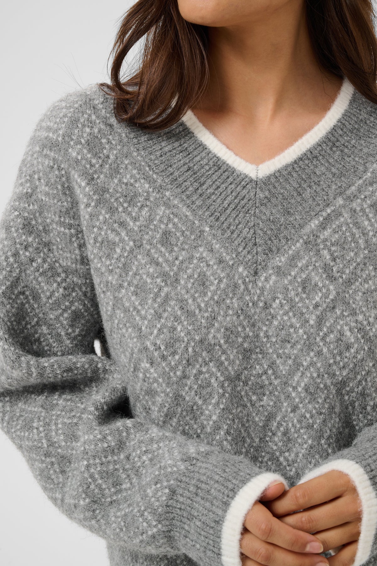 A close-up of a woman wearing a gray knit sweater with a white V-neck trim and white ribbed cuffs.