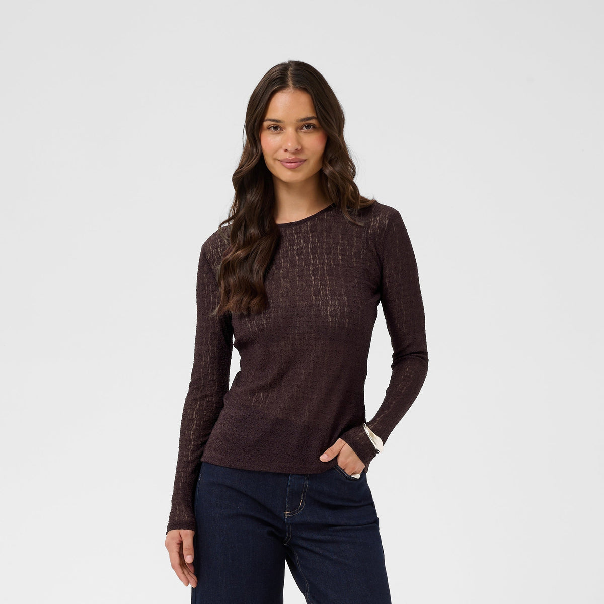 Woman wearing a dark brown long-sleeve top and dark blue jeans on a white background