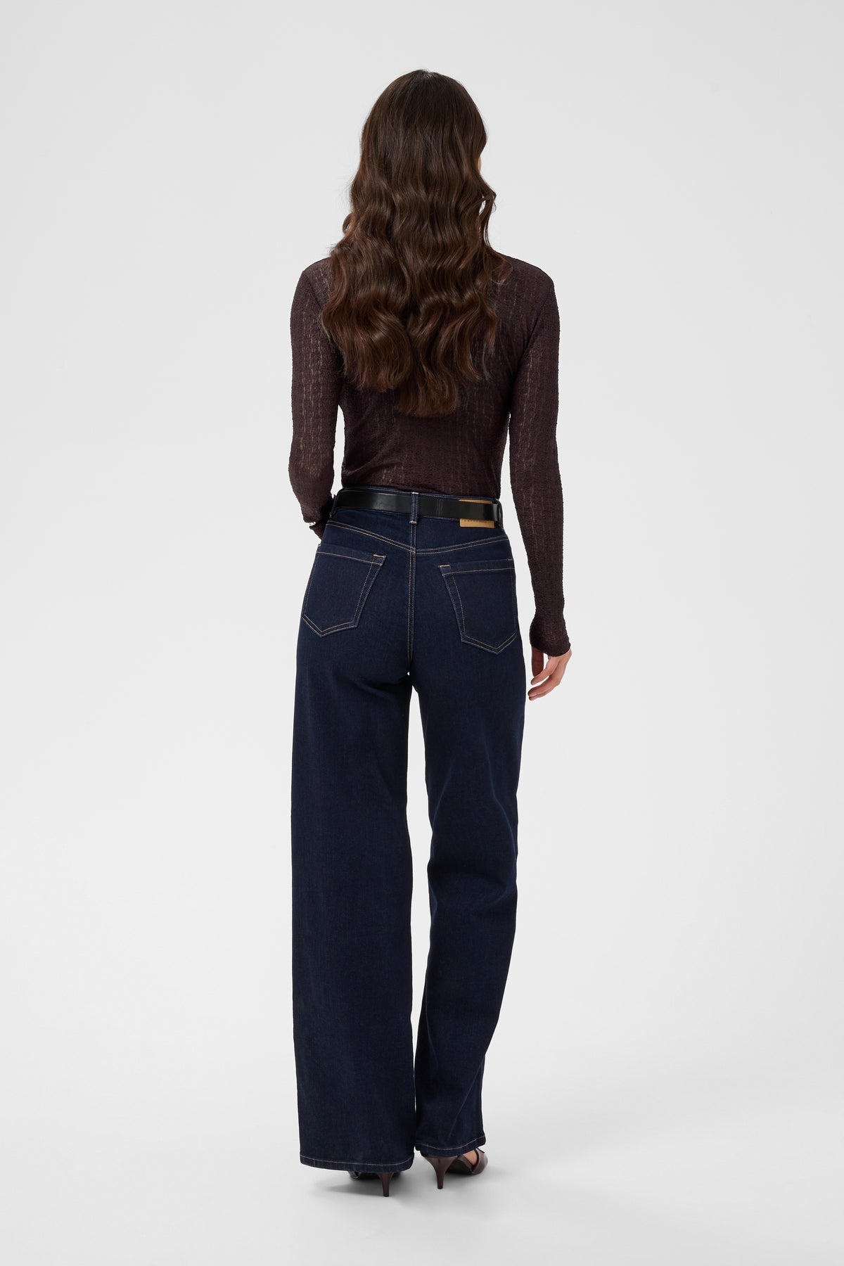 Person wearing dark blue jeans and a brown top on a white background