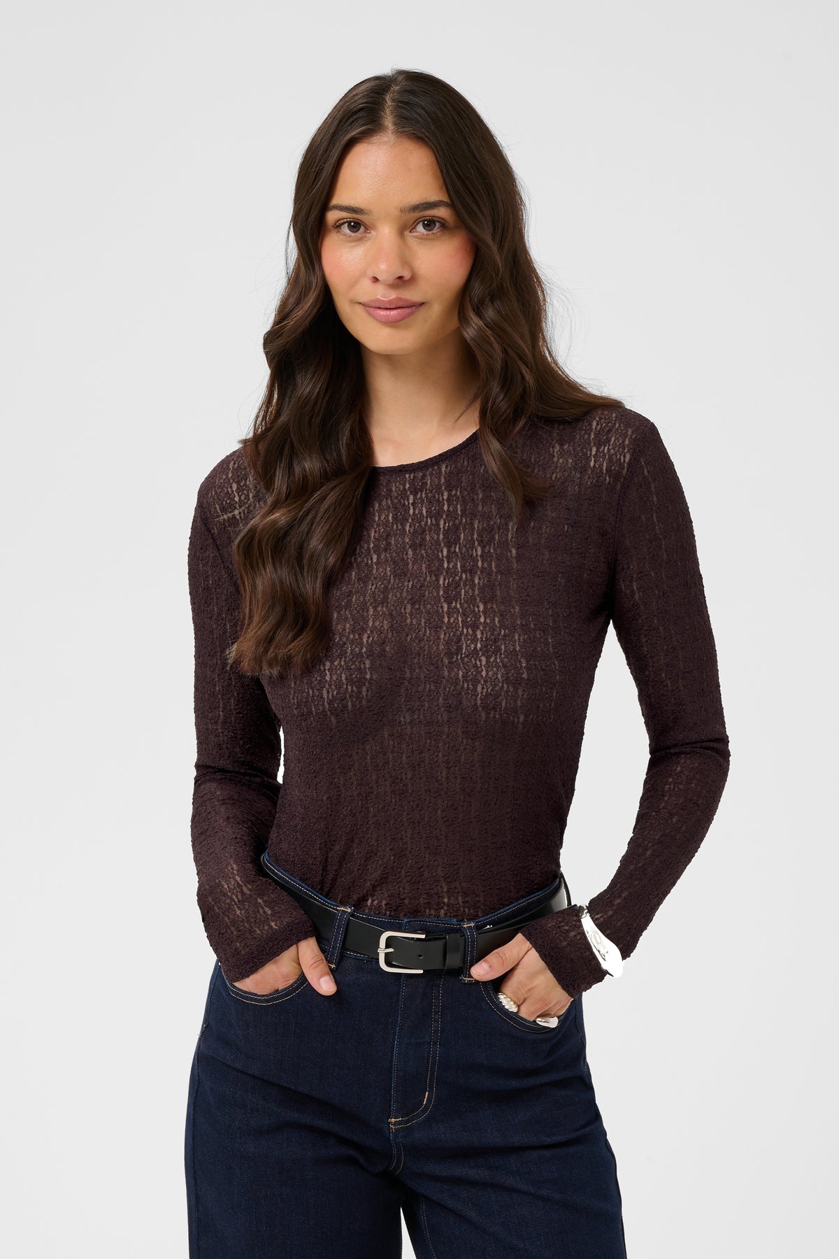 Woman wearing a dark brown long-sleeve top and blue jeans on a white background