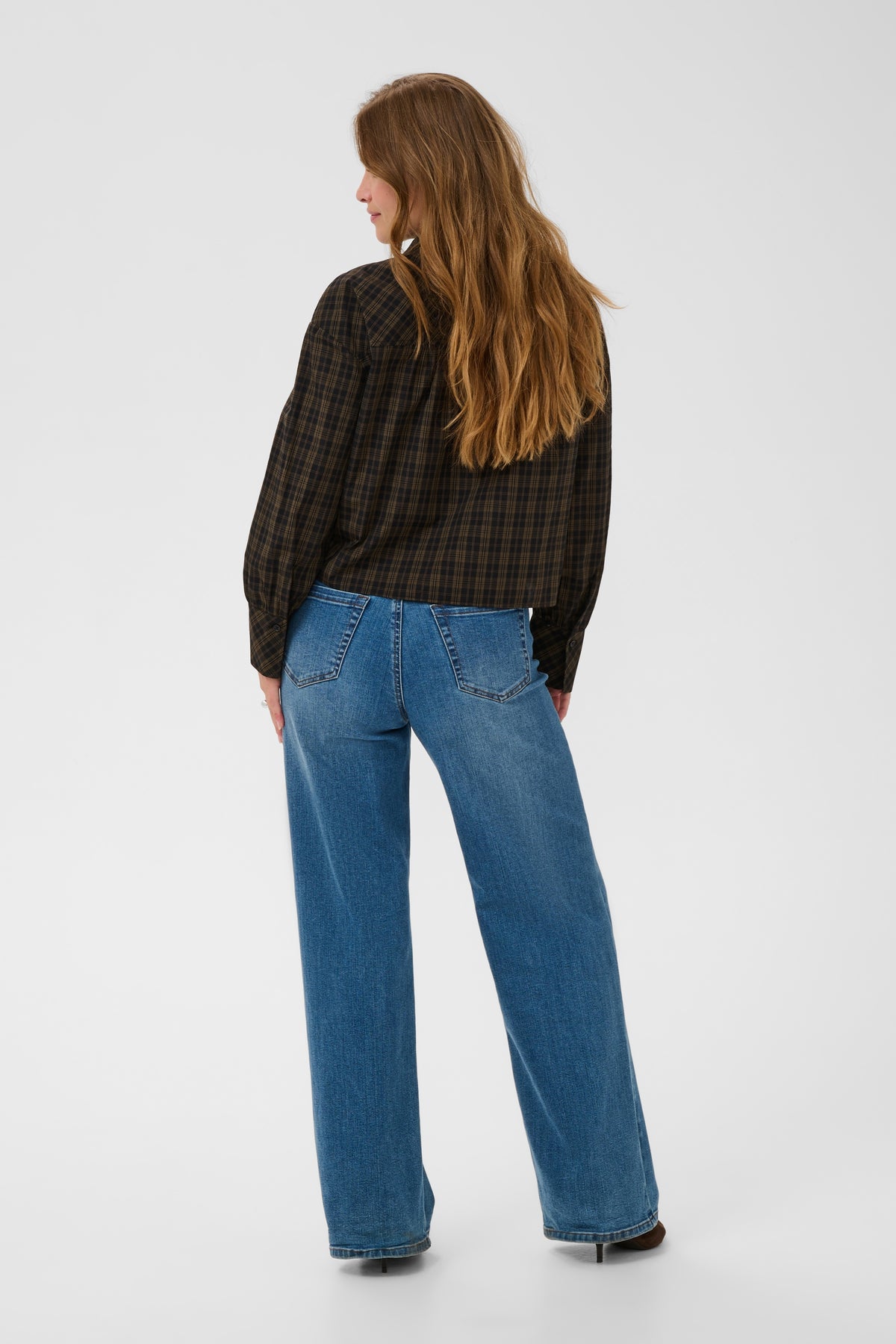 Person wearing blue jeans and a black plaid shirt on a white background
