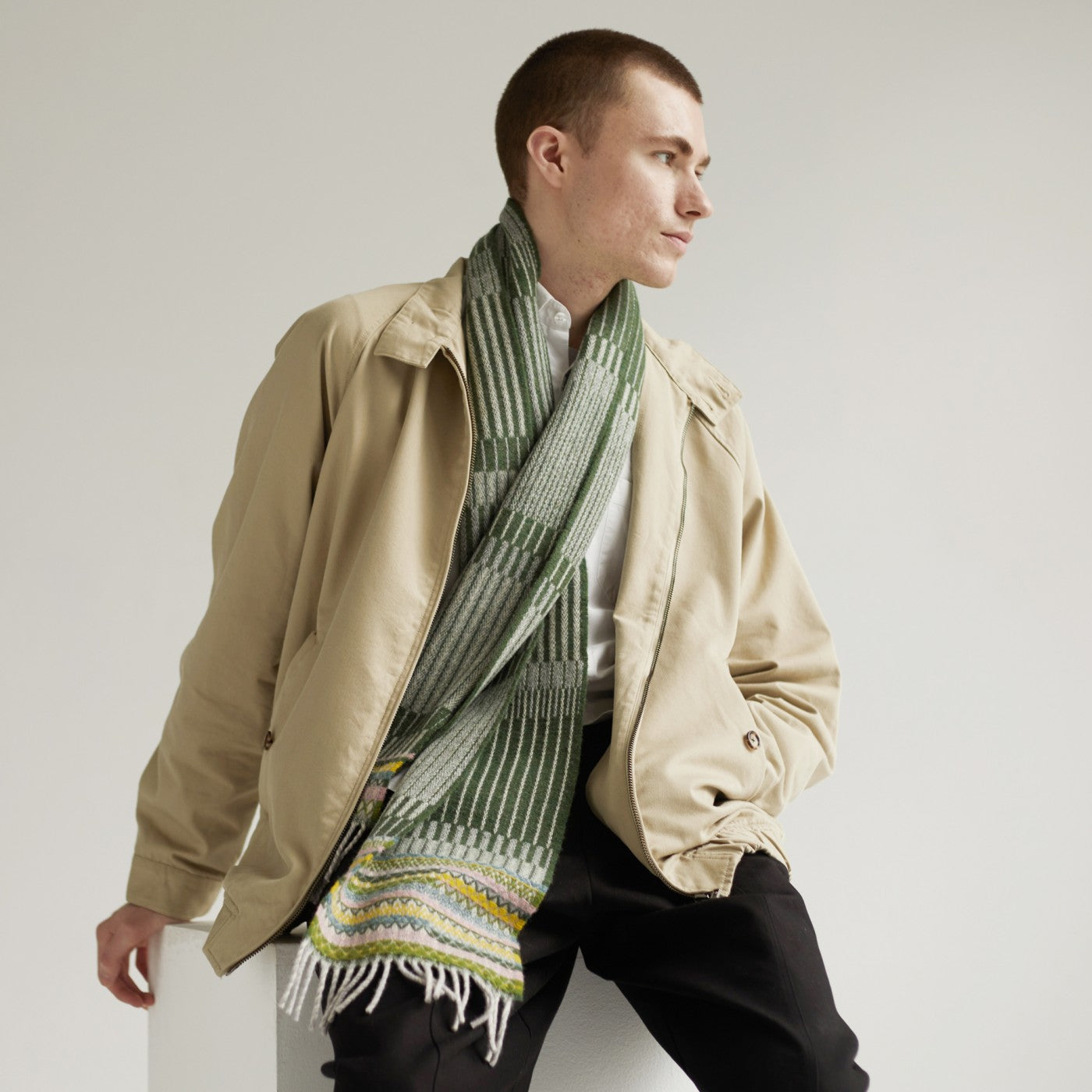 Man wearing a tan jacket and a green and white patterned scarf.