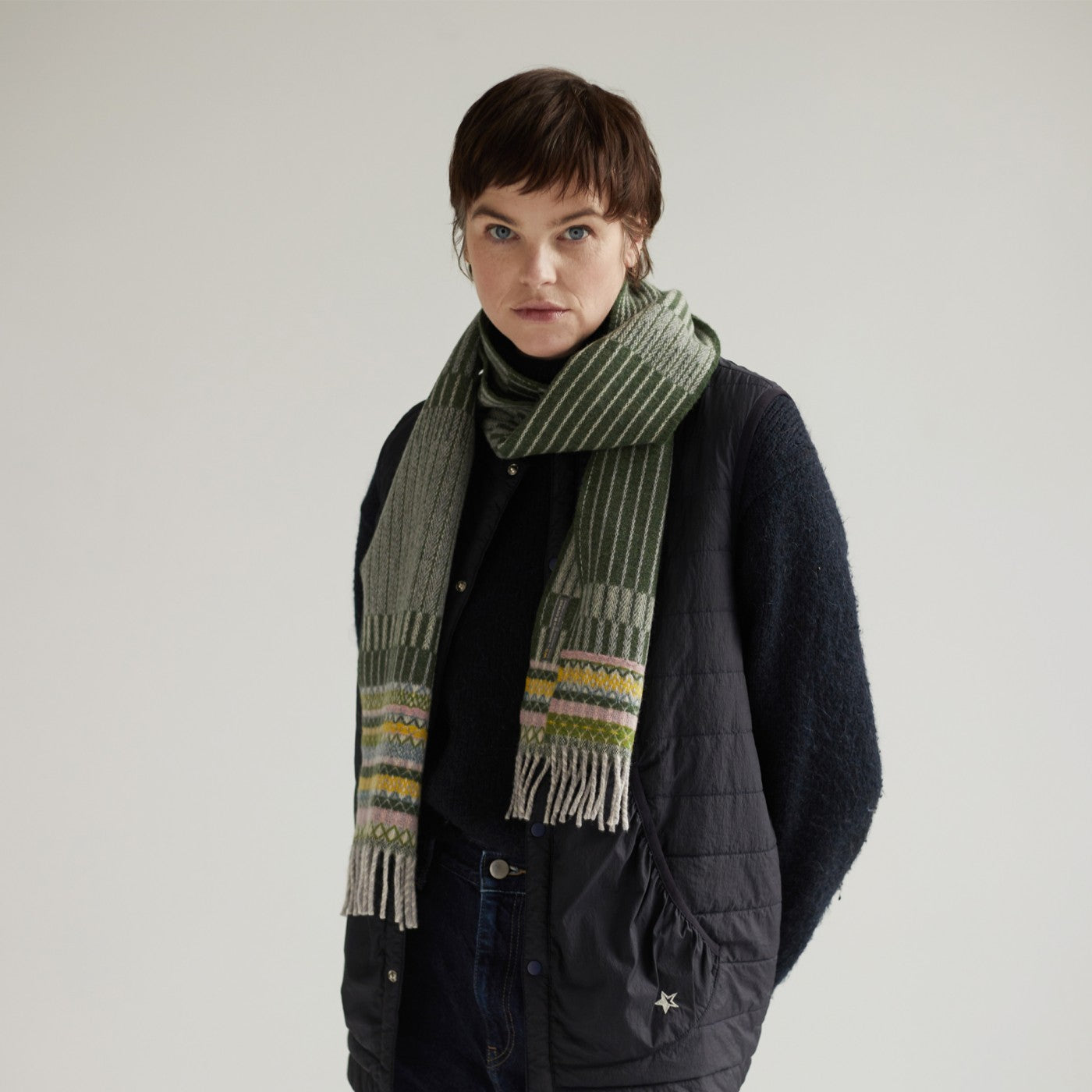 A green and beige striped scarf with multicolored woven details and fringed ends.