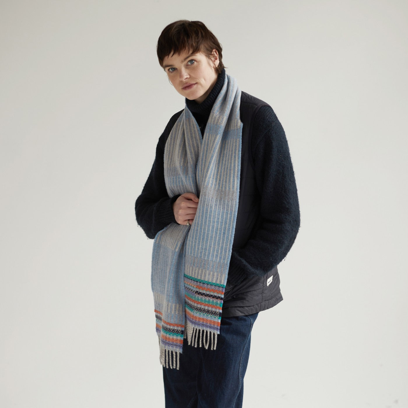 Light blue and cream striped wool scarf with multicolored woven detail at the bottom and fringed edges.