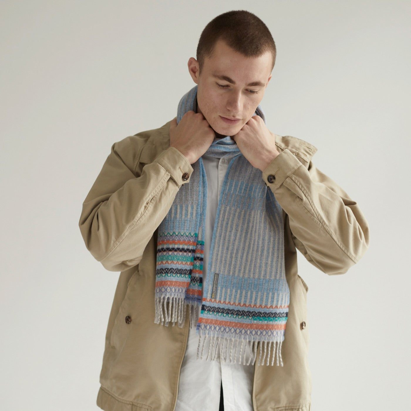 Light blue and beige patterned wool scarf with multicolored woven accents and fringed edges.