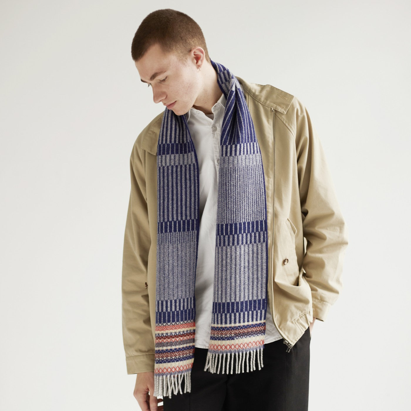 A blue and gray patterned wool scarf with fringed edges, worn over a beige jacket.