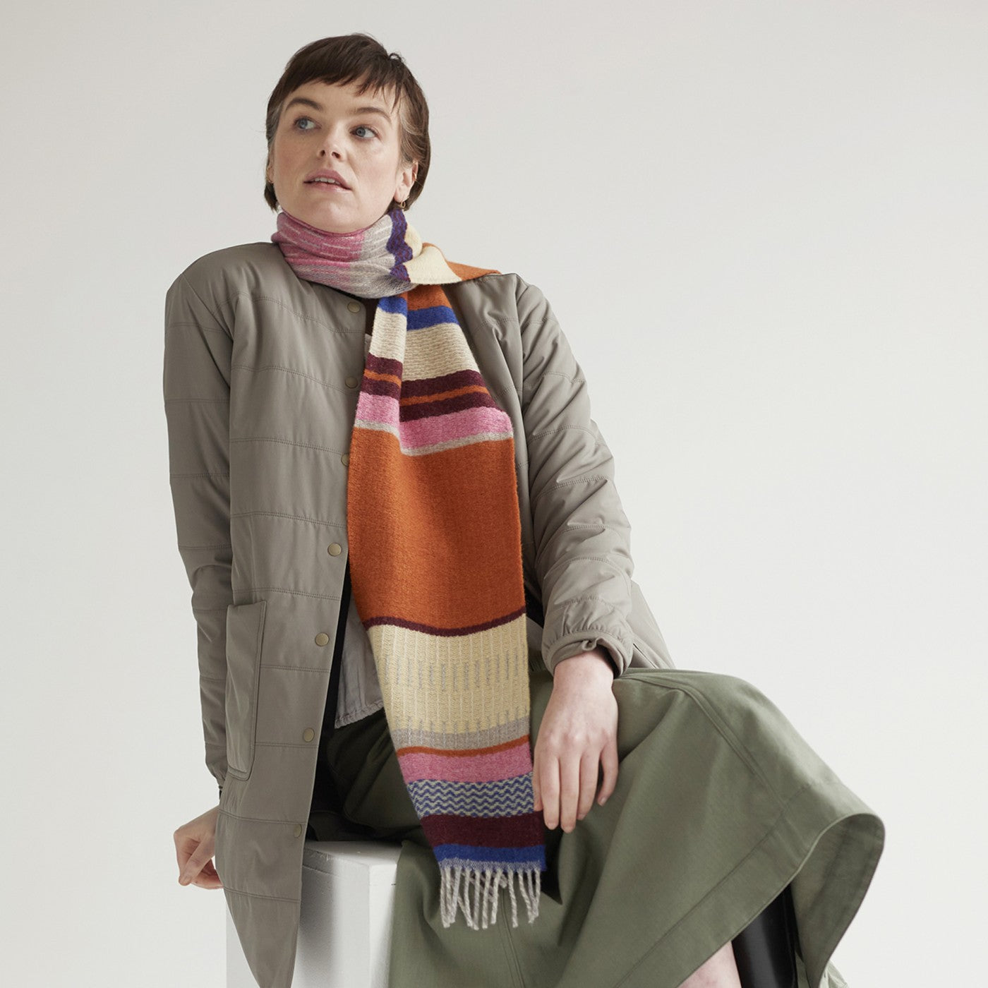 A woman wearing a taupe quilted jacket and a multicolored striped scarf.
