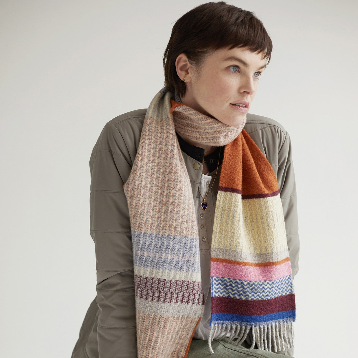 Multicolored striped wool scarf with fringe, featuring peach, orange, cream, pink, and blue tones.