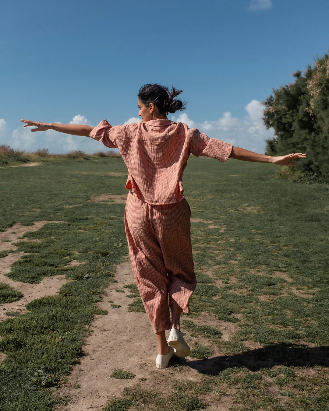 Woman in a pink outfit standing with arms outstretched in a grassy field.
