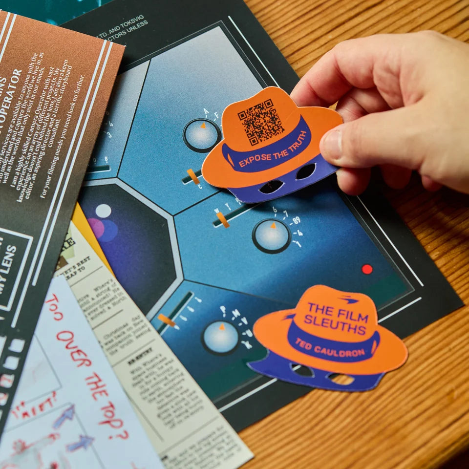 A hand holds a die-cut sticker shaped like a fedora hat over a printed film quiz card. The sticker is orange and purple with a QR code and text reading 'EXPOSE THE TRAP' and 'THE FILM SLEUTHS TED CAULDRON.