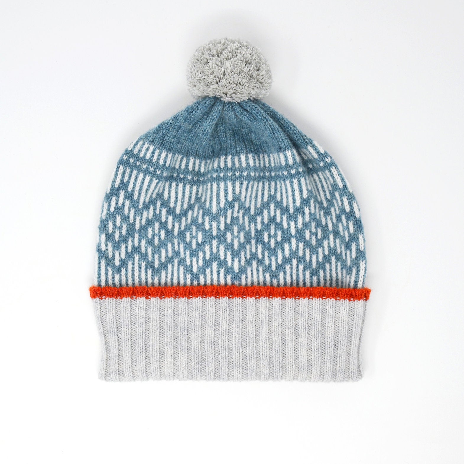 Knitted beanie with a gray pompom, teal and white patterned crown, and orange and gray ribbed cuff.