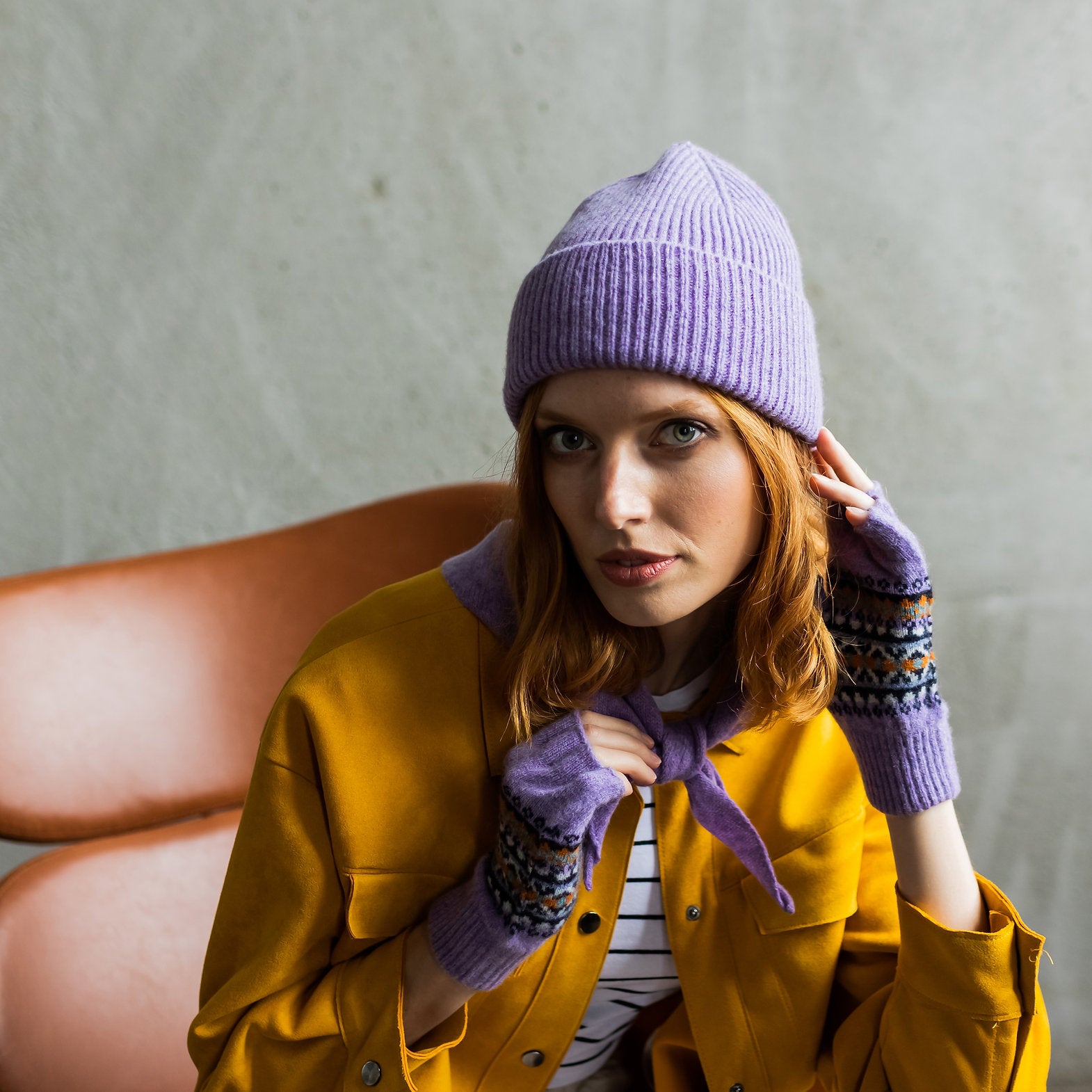 Woman wearing a lavender ribbed beanie, matching fingerless gloves with patterned cuffs, and a mustard yellow jacket.