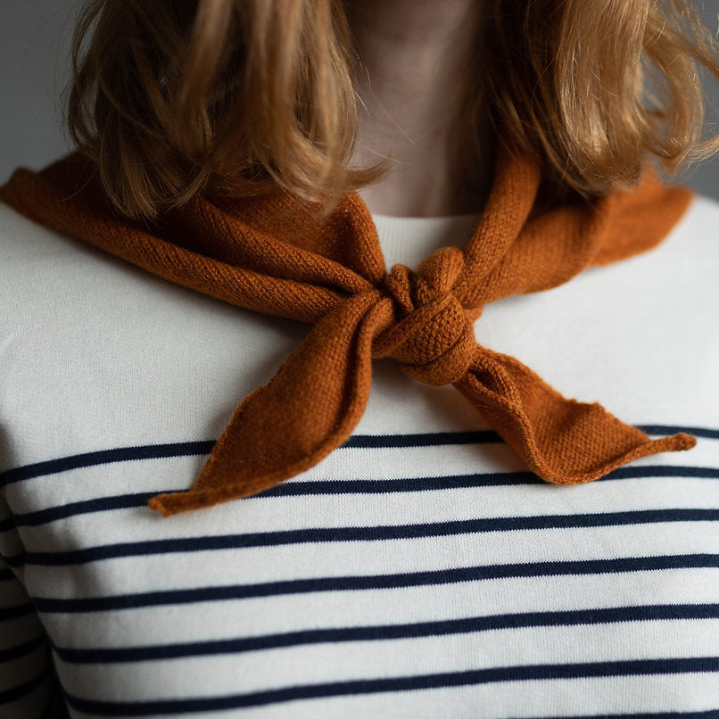 Burnt orange knitted neck scarf tied in a bow.