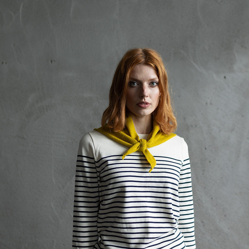 Woman wearing a cream and navy striped long-sleeve shirt with a mustard yellow neck scarf.