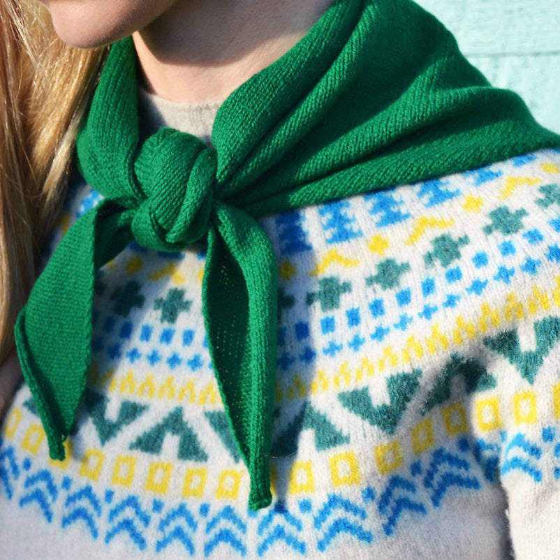 Bright green knitted neck scarf tied in a bow, worn over a cream sweater with a colorful Fair Isle pattern.