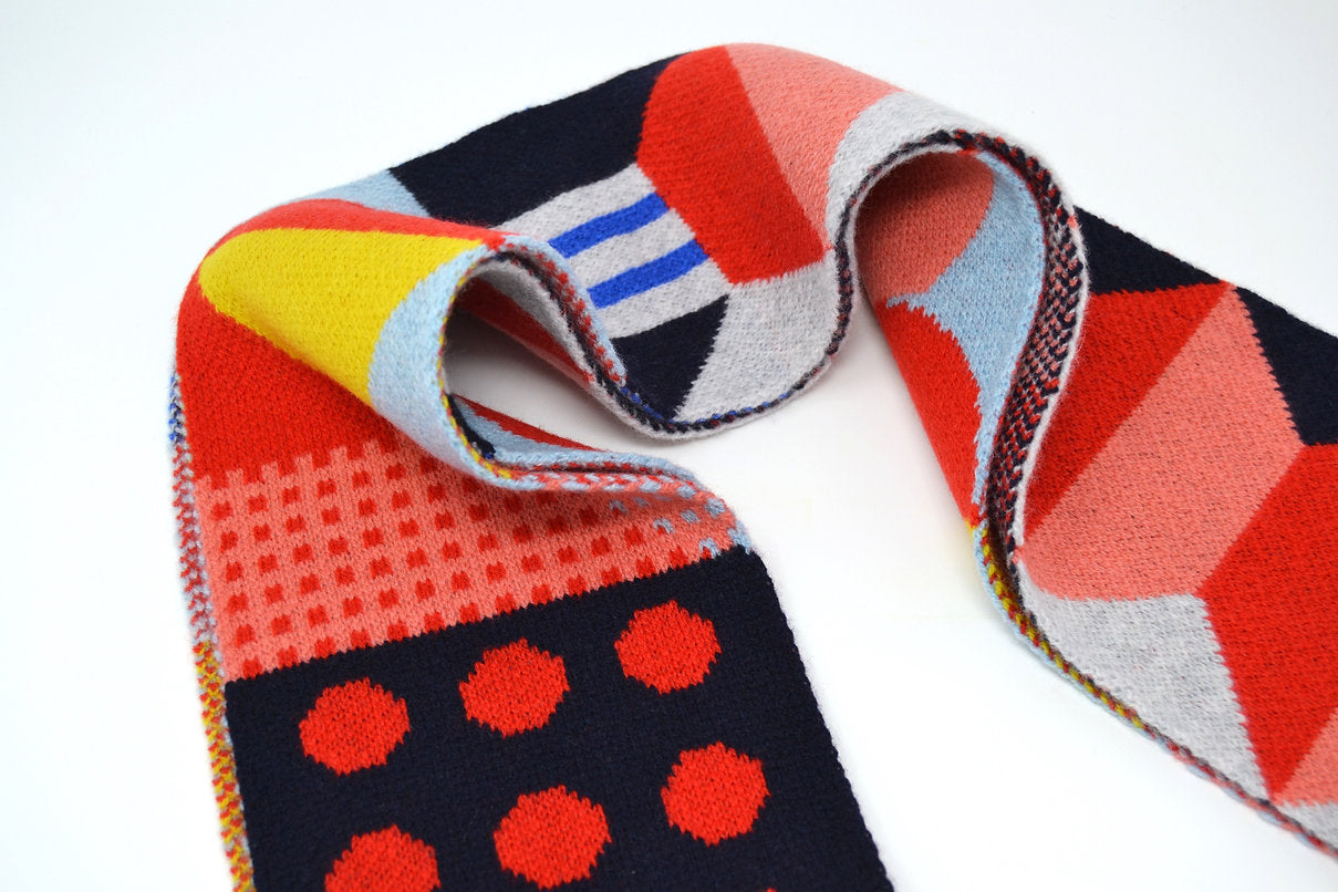 Multicolored knit scarf with geometric patterns in red, pink, yellow, blue, and navy.