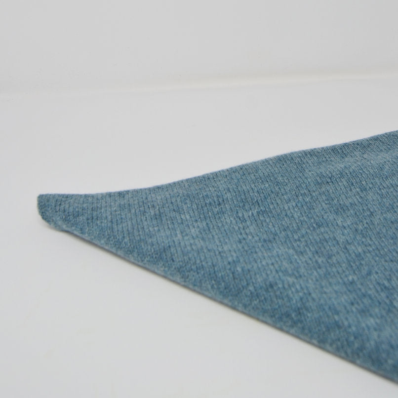 Light blue knitted fabric swatch, triangular shape, textured surface.