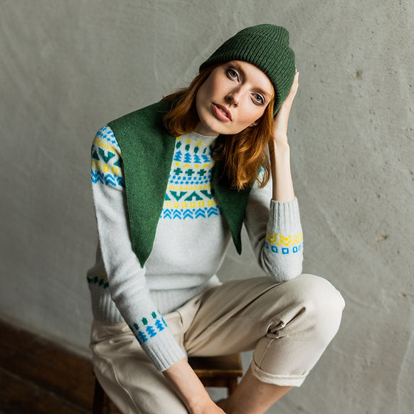 Fair isle-patterned cream sweater with green and blue details, worn with a dark green beanie.