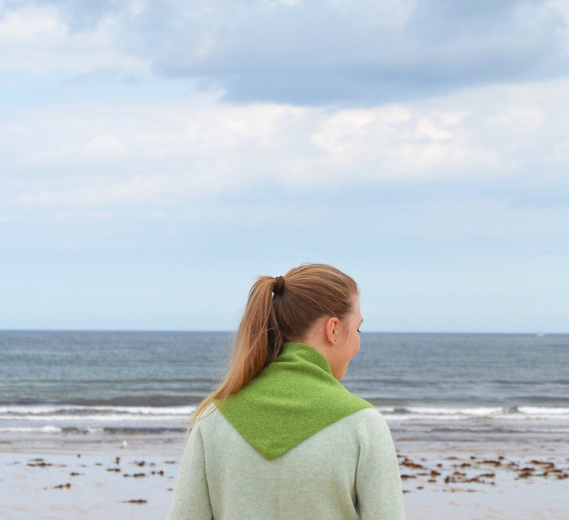 Person wearing a green sweater on a beach with ocean and sky in the background