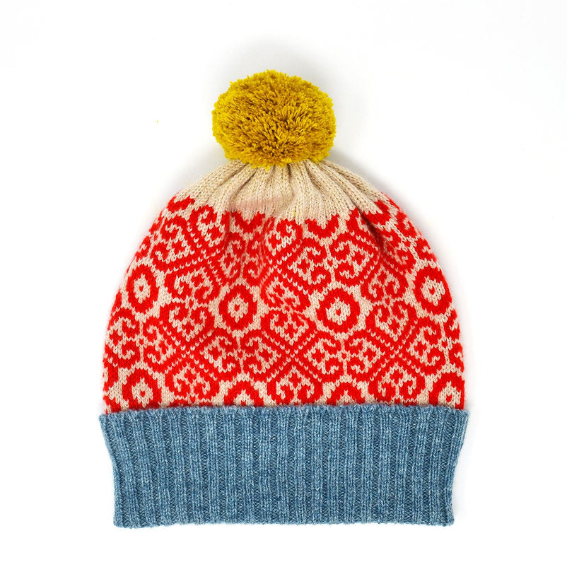 Knit beanie with red and cream patterned crown, blue ribbed cuff, and yellow pompom.