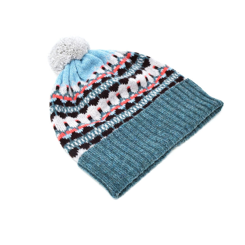 Knit winter hat with pompom, featuring a teal base and a patterned crown in shades of blue, white, black, and coral.