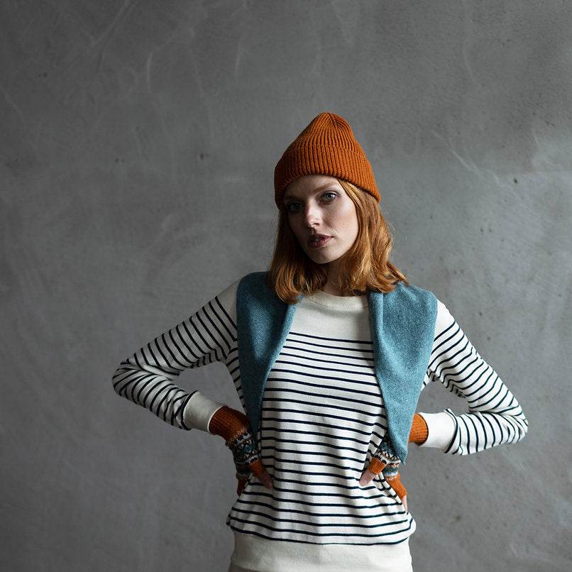 Woman wearing a rust-colored beanie, striped sweater, teal shawl, and patterned fingerless gloves.