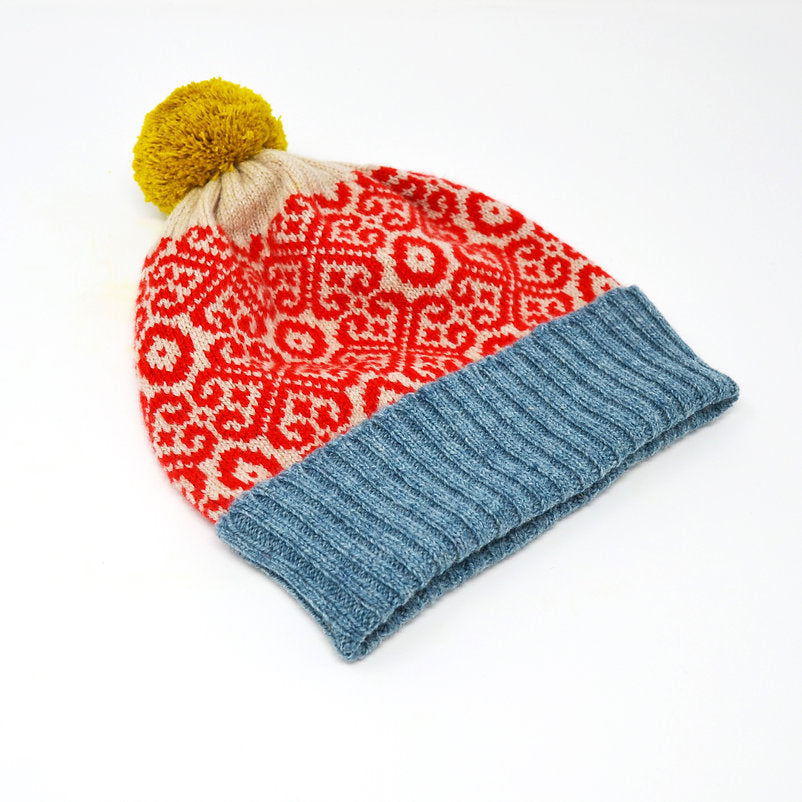 Knit beanie with red and cream patterned crown, blue ribbed cuff, and yellow pompom.