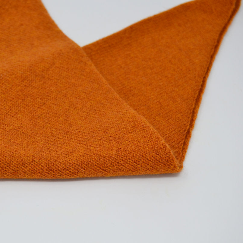 Close-up of a folded, burnt orange knit scarf.  The fabric has a soft, textured appearance.
