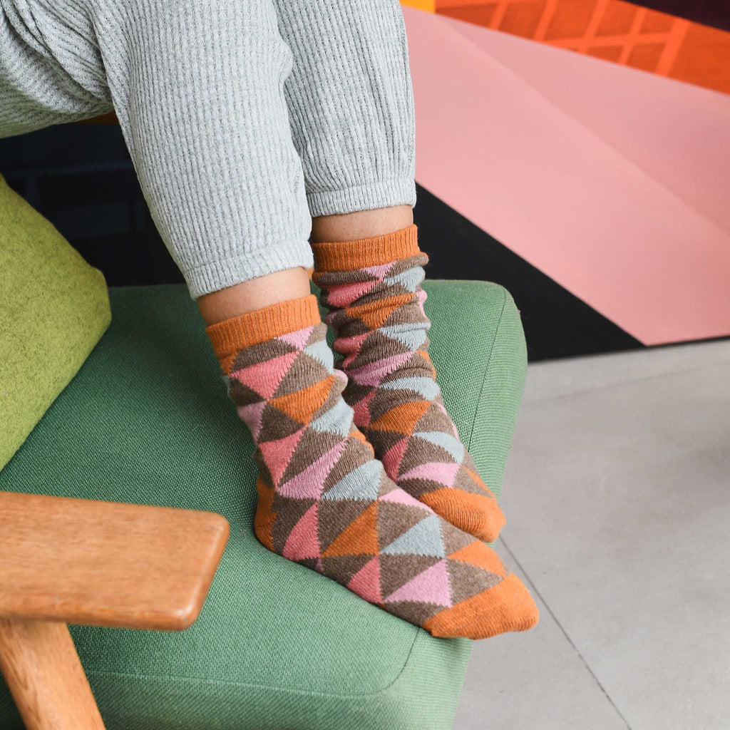 Pair of mid-calf socks with a geometric pattern in shades of orange, pink, brown, and gray.